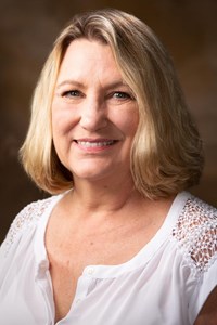 White woman with shoulder-length, bob-style blond hair, wearing white shirt and smiling at the camera