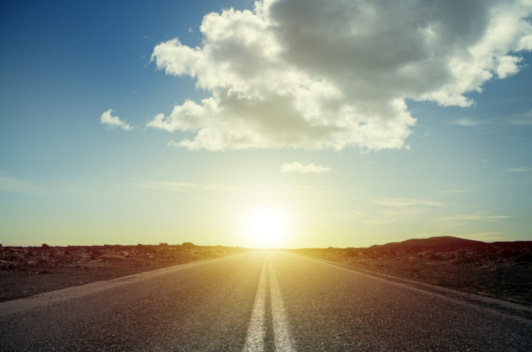 Color photo of double lane highway going into the sunset