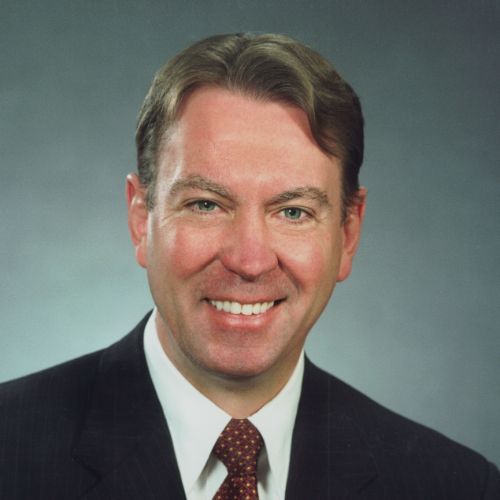 A man in a black suit smiles as he poses for a portrait