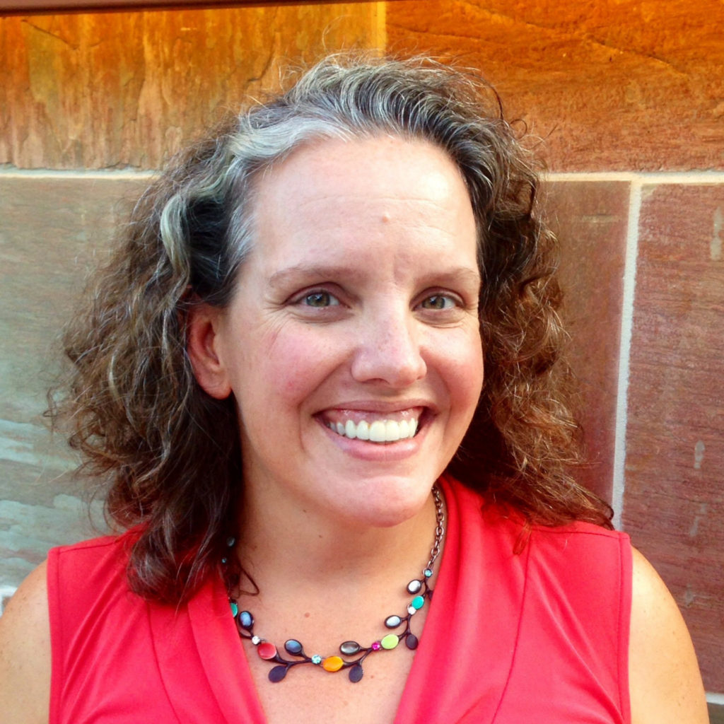 A woman with curly hair and a red shirt smiles for a portrait