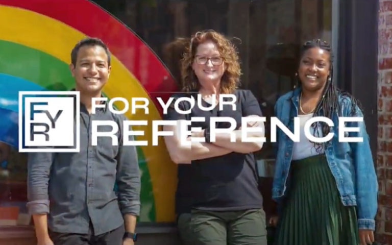 Color photo of three people standing in row leaning on a window with rainbow decal.