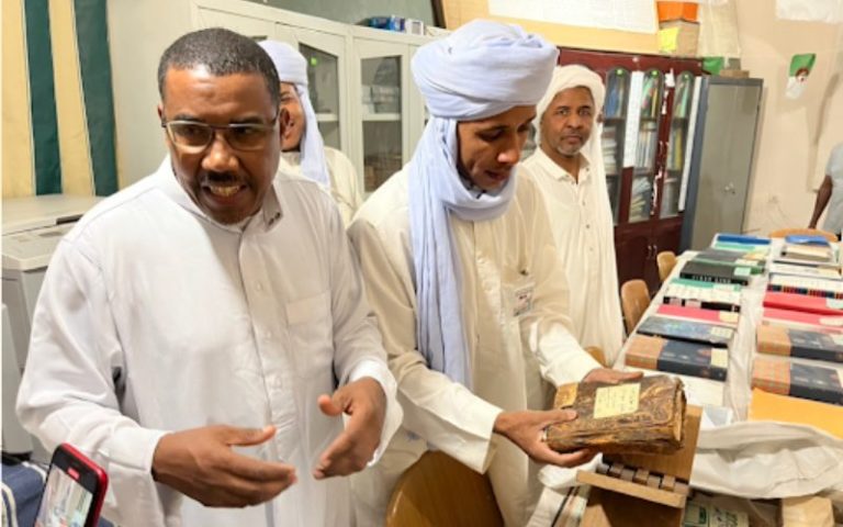 Three members of the Algerian Khizana stand in front of a collection of manuscripts on long table.