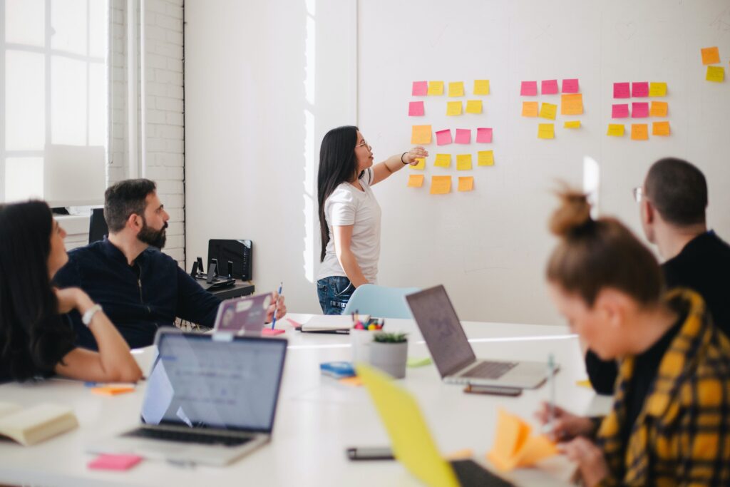 Woman placing sticky notes on wall in front of a conference table full of colleagues