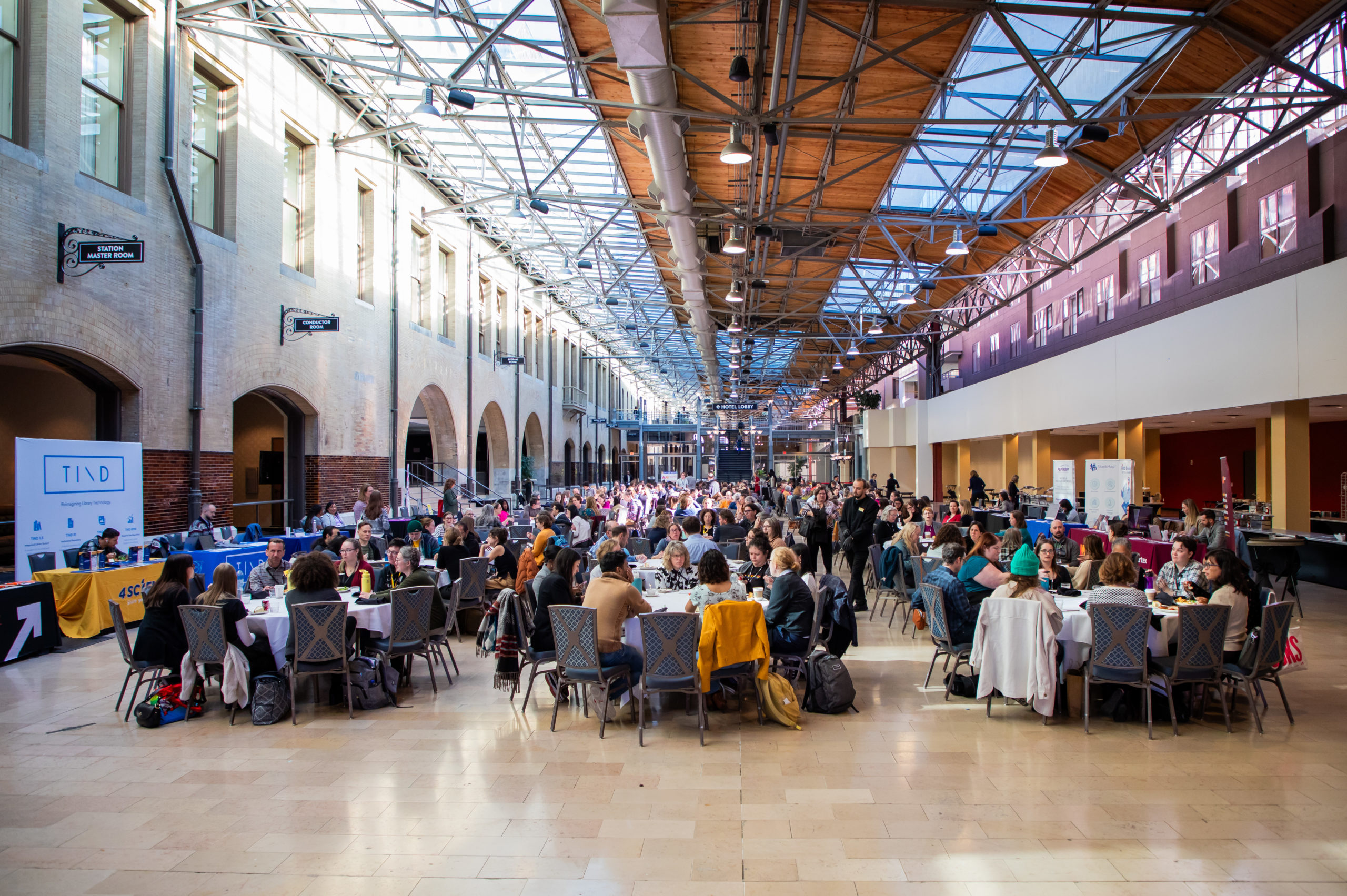 Wide angle view of people seated inside large hotel hall at round tables.