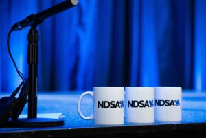 A microphone and three NDSA mugs in a row on a stage